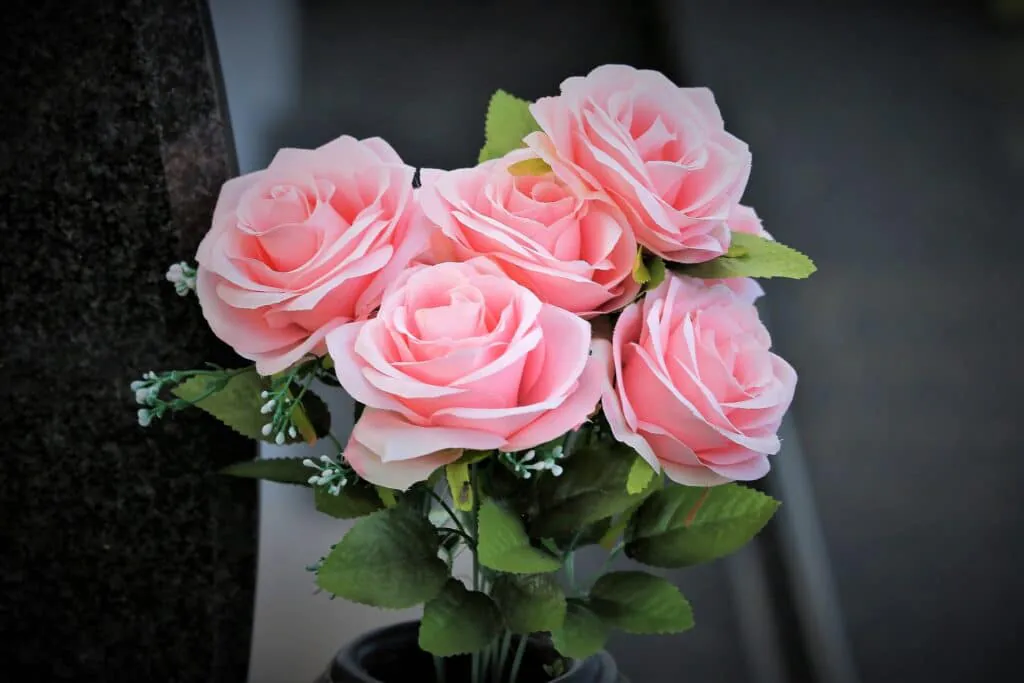 Strauß künstlicher rosa Rosen neben einem Grabstein, Symbol für Gedenken