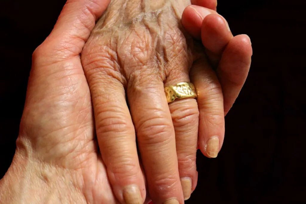 Nahaufnahme einer älteren Hand mit Goldring, die liebevoll von einer anderen Hand gehalten wird – Symbol für Unterstützung und Fürsorge